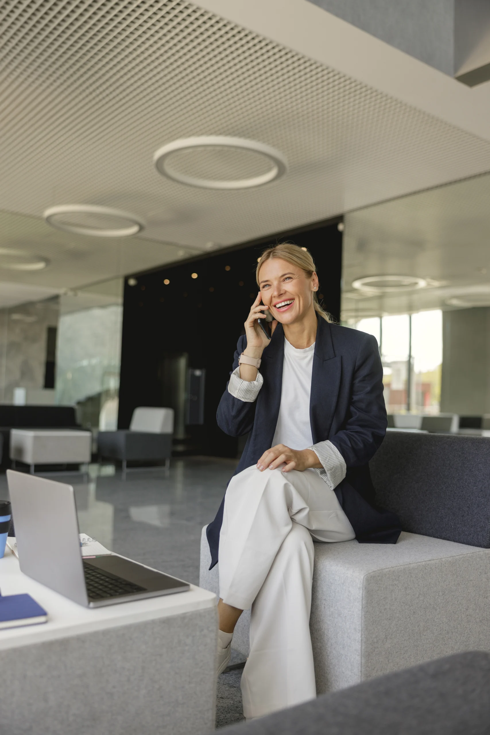 cheerful-businesswoman-talking-phone-sitting-background-modern-offfice-looks-away